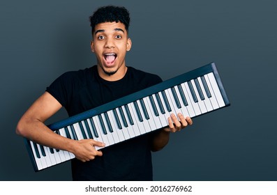 Young african american man holding piano keyboard celebrating crazy and amazed for success with open eyes screaming excited.  - Powered by Shutterstock