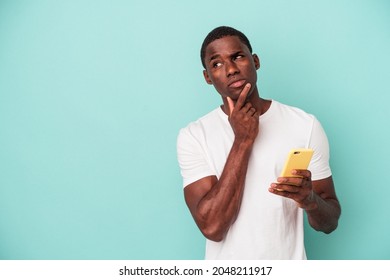 Young African American man holding a mobile phone isolated on blue background looking sideways with doubtful and skeptical expression. - Shutterstock ID 2048211917