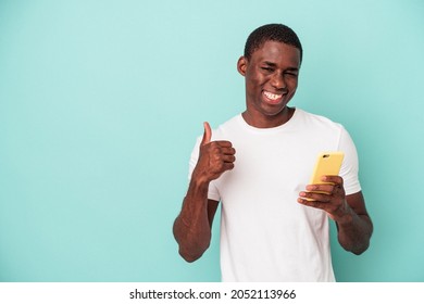 Young African American Man Holding A Mobile Phone Isolated On Blue Background Smiling And Raising Thumb Up