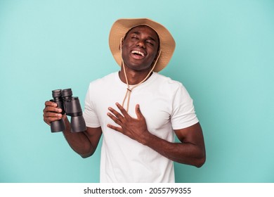 Young African American Man Holding Binoculars Isolated On Blue Background Laughs Out Loudly Keeping Hand On Chest.