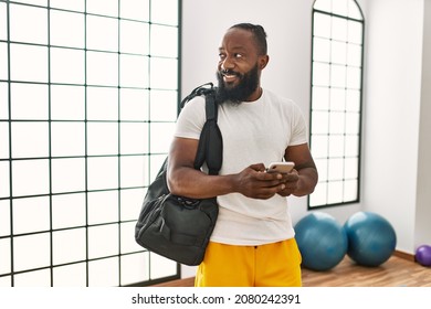 Young African American Man Holding Gym Bag Using Smartphone At Sport Center