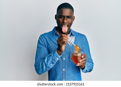 Young African American Man Holding Honey Sticking Tongue Out Happy With Funny Expression. 