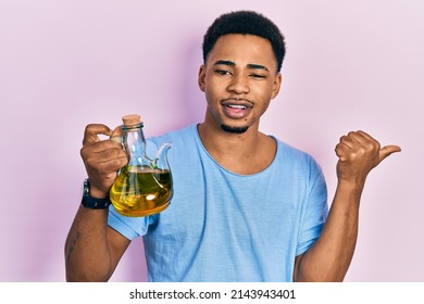 Young African American Man Holding Olive Oil Can Pointing Thumb Up To The Side Smiling Happy With Open Mouth 