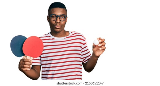 Young african american man holding red ping pong rackets and ball looking at the camera blowing a kiss being lovely and sexy. love expression. 