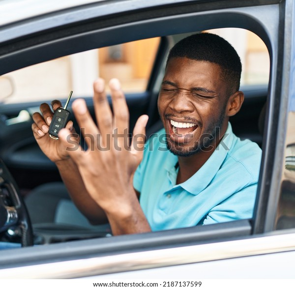 Young african american man holding\
key of new car with cheerful expression at\
street