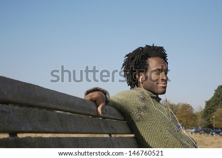 Young African American man listening to music while sitting on park bench
