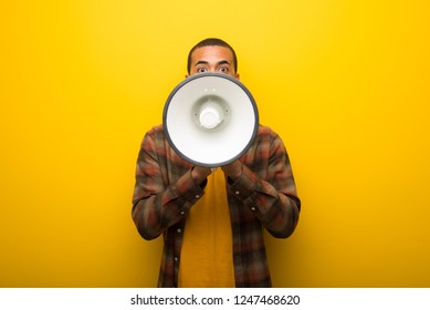 Young African American Man On Vibrant Yellow Background Shouting Through A Megaphone To Announce Something