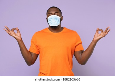 Young african american man in orange t-shirt sterile face mask safe from coronavirus virus covid-19 hold hands in yoga gesture relaxing meditating isolated on pastel violet background studio portrait - Powered by Shutterstock