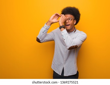 Young African American Man Over An Orange Wall Making The Gesture Of A Spyglass