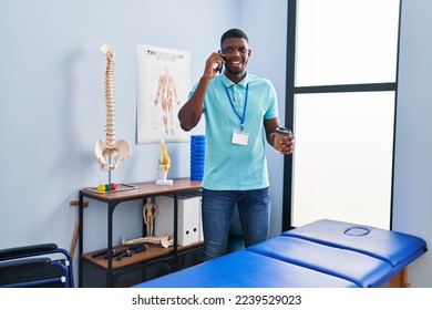 Young african american man physiotherapist talking on the smartphone and drinking coffee al rehab clinic - Powered by Shutterstock