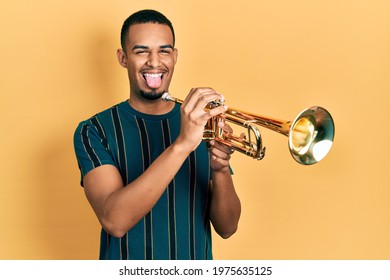 Young African American Man Playing Trumpet Sticking Tongue Out Happy With Funny Expression. 