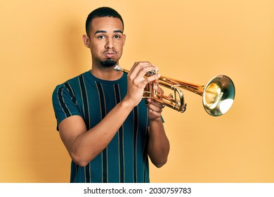 Young African American Man Playing Trumpet Puffing Cheeks With Funny Face. Mouth Inflated With Air, Catching Air. 