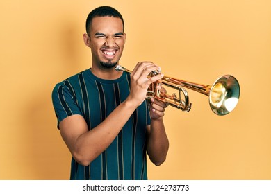 Young African American Man Playing Trumpet Smiling And Laughing Hard Out Loud Because Funny Crazy Joke. 