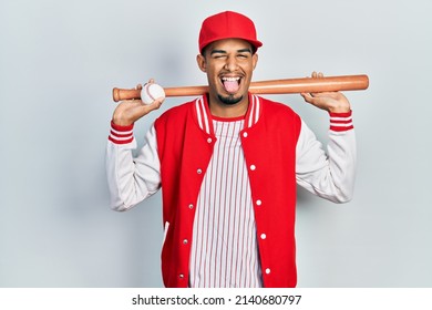 Young african american man playing baseball holding bat and ball sticking tongue out happy with funny expression.  - Powered by Shutterstock