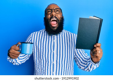 Young African American Man Reading Book And Drinking A Cup Of Coffee Angry And Mad Screaming Frustrated And Furious, Shouting With Anger Looking Up. 