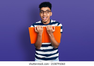 Young African American Man Reading A Book With Glasses Smiling And Laughing Hard Out Loud Because Funny Crazy Joke. 