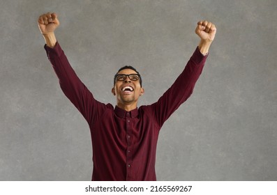 Young african american man screaming clenching fist standing with raised hands up looking up studio shot. Black guy celebrating win, rejoicing success and goal achievement. People positive emotion