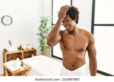 Young african american man shirtless wearing towel standing at beauty center surprised with hand on head for mistake, remember error. forgot, bad memory concept. 