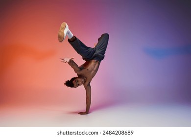 A young African American man, shirtless and wearing grey pants, performs a handstand on a vibrant gradient backdrop. - Powered by Shutterstock