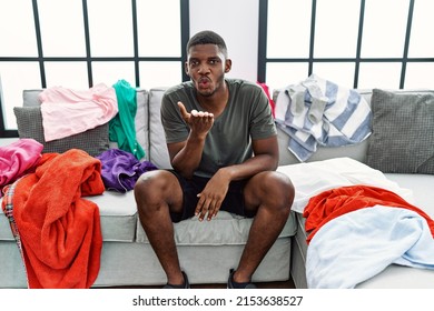 Young African American Man Sitting On The Sofa With Dirty Laundry Clothes Looking At The Camera Blowing A Kiss With Hand On Air Being Lovely And Sexy. Love Expression. 