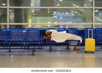 Young African American man sleeping under plaid, waiting for flight, feel cold. Black guy lying on chairs in airport lounge, sleep on an uncomfortable bench, freezing. Long night connection. 
