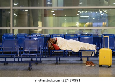 Young African American Man Sleeping Under Plaid, Waiting For Flight, Feel Cold. Black Guy Lying On Chairs In Airport Lounge, Sleep On An Uncomfortable Bench, Freezing. Long Night Connection. 