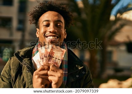 Young african american man smiling happy  holding south africa rands banknotes at the city