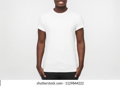 Young African American Man Standing With Hands In Pockets, Wearing Blank White T Shirt With Copy Space For Your Logo Or Text, Isolated On Grey Background