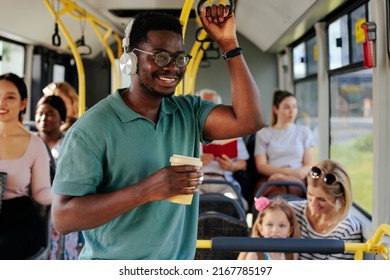 Young african american man standing in the bus, with coffee in his hand, looking through the window and smiling - Powered by Shutterstock