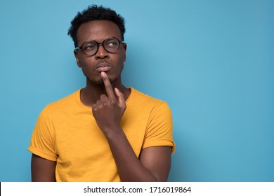 Young african american man, student with finger in mouth in deep thought, isolated on blue background. Negative emotion, facial expression, feelings - Powered by Shutterstock