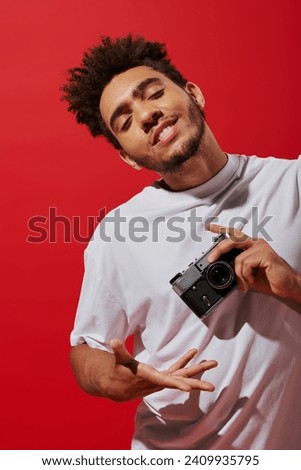 young african american man taking shot on retro camera and smiling on red background, creative