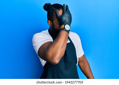 Young African American Man Tattoo Artist Wearing Professional Uniform And Gloves Surprised With Hand On Head For Mistake, Remember Error. Forgot, Bad Memory Concept. 