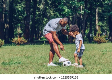 young african american man teaching adorable son playing football in park
