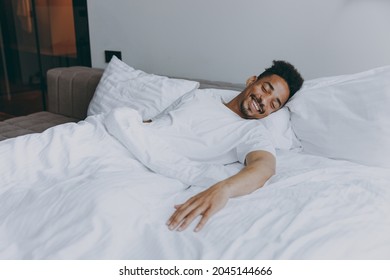 Young african american man wear nightwear take nap sleeping lying in bed rest relax spend time in bedroom lounge home in own room house wake up dream be lost in reverie good day. Real estate concept. - Shutterstock ID 2045144666