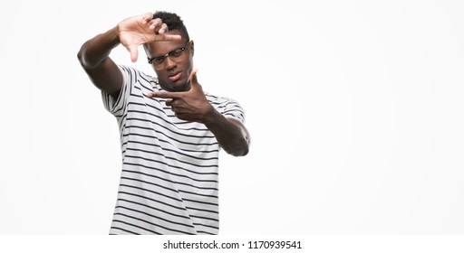 Young African American Man Wearing Glasses And Navy T-shirt Smiling Making Frame With Hands And Fingers With Happy Face. Creativity And Photography Concept.