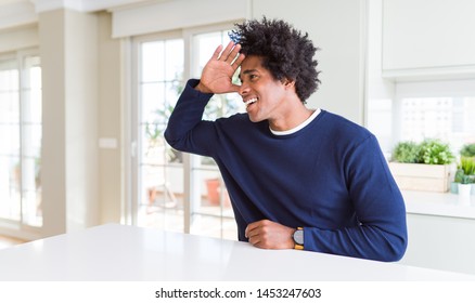 Young african american man wearing casual sweater sitting at home very happy and smiling looking far away with hand over head. Searching concept. - Shutterstock ID 1453247603