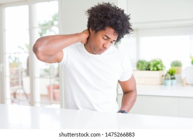 Young african american man wearing casual white t-shirt sitting at home Suffering of neck ache injury, touching neck with hand, muscular pain