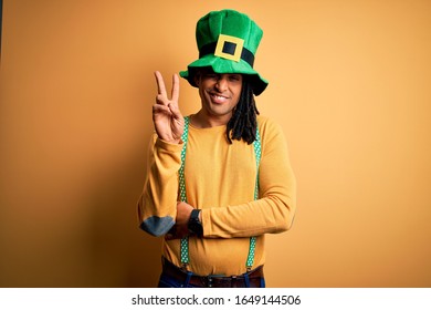 Young african american man wearing green hat celebrating saint patricks day smiling with happy face winking at the camera doing victory sign. Number two.