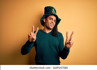 Young african american man wearing green hat with clover celebrating saint patricks day smiling looking to the camera showing fingers doing victory sign. Number two.