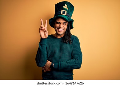 Young african american man wearing green hat with clover celebrating saint patricks day smiling with happy face winking at the camera doing victory sign. Number two.