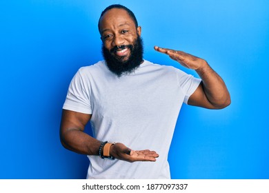 Young African American Man Wearing Casual White Tshirt Gesturing With Hands Showing Big And Large Size Sign, Measure Symbol. Smiling Looking At The Camera. Measuring Concept. 