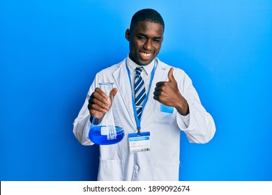 Young African American Man Wearing Scientist Uniform Holding Test Tube Smiling Happy And Positive, Thumb Up Doing Excellent And Approval Sign 