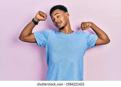 Young african american man wearing casual blue t shirt stretching back, tired and relaxed, sleepy and yawning for early morning  - Shutterstock ID 1984221425