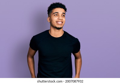 Young African American Man Wearing Casual Black T Shirt Looking To Side, Relax Profile Pose With Natural Face And Confident Smile. 