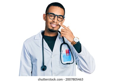 Young African American Man Wearing Doctor Uniform And Stethoscope Pointing With Hand Finger To Face And Nose, Smiling Cheerful. Beauty Concept 