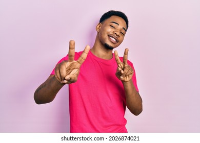 Young african american man wearing casua t shirt smiling looking to the camera showing fingers doing victory sign. number two. 