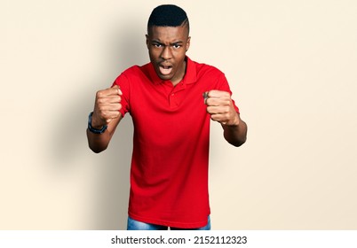 Young African American Man Wearing Casual Red T Shirt Angry And Mad Raising Fists Frustrated And Furious While Shouting With Anger. Rage And Aggressive Concept. 