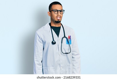 Young african american man wearing doctor uniform and stethoscope in shock face, looking skeptical and sarcastic, surprised with open mouth  - Shutterstock ID 2168239331