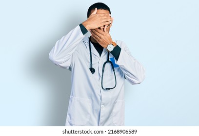 Young African American Man Wearing Doctor Uniform And Stethoscope Covering Eyes And Mouth With Hands, Surprised And Shocked. Hiding Emotion 