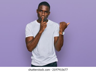 Young african american man wearing casual white t shirt asking to be quiet with finger on lips pointing with hand to the side. silence and secret concept. 